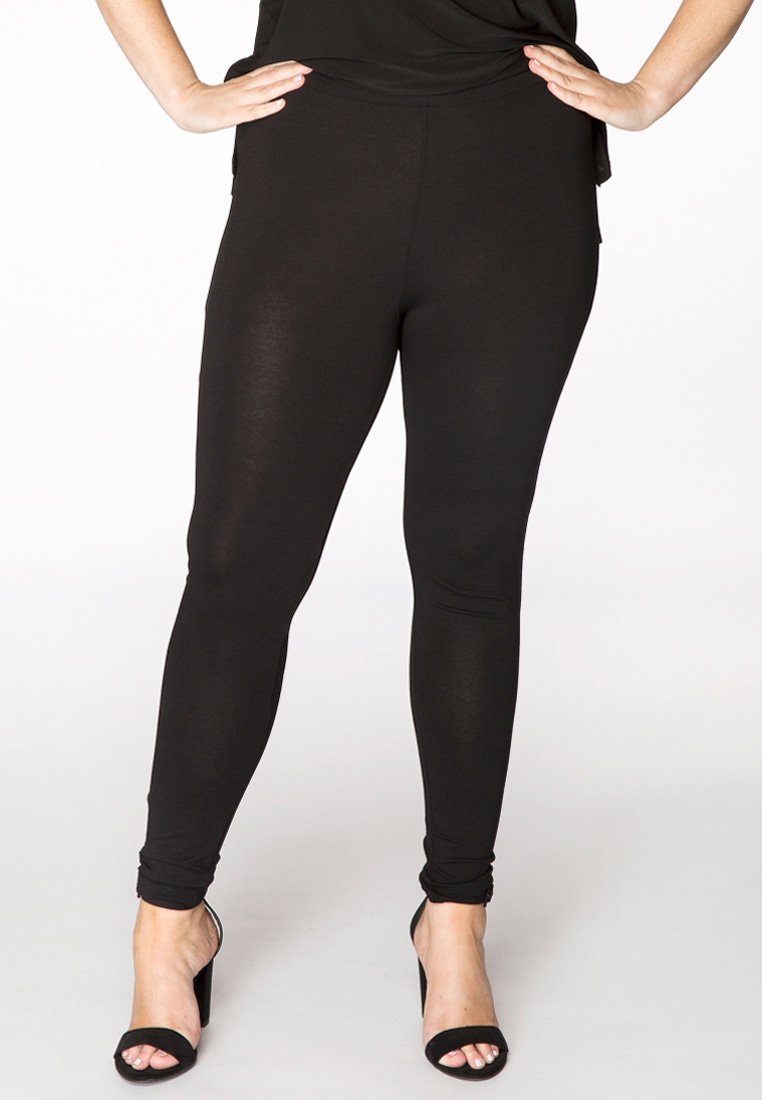 Zwarte legging van rekbare stof, slim fit ontwerp, gladde textuur en enkelhoogte, gecombineerd met zwarte hoge hakken sandalen.