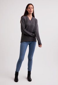 Maglione grigio a collo a V con orlo a coste, realizzato in morbido tessuto a maglia. Abbinato a jeans skinny azzurri e stivali neri alla caviglia.