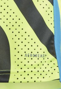Tejido de patrón amarillo y negro con pequeños puntos, que presenta un logo que dice "AEROREADY" en gris. Diseño texturizado y atlético.