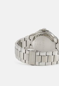Reloj de acero inoxidable con un diseño elegante, que presenta una pulsera pulida, eslabones cepillados y una corona prominente. Logo grabado en el cierre.