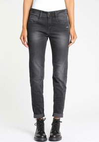Jeans negros ajustados de mezclilla, con un diseño clásico de cinco bolsillos y puños enrollados, combinados con botas negras de cordones.