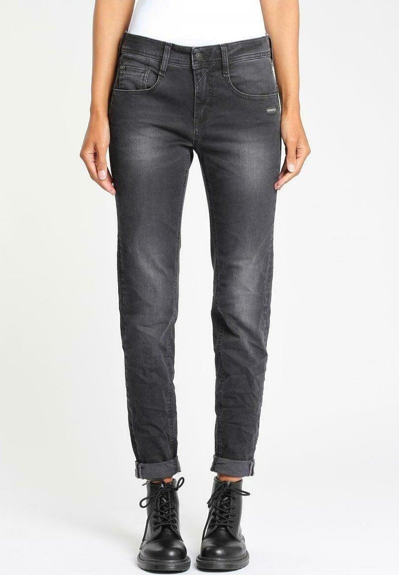Jeans negros ajustados de mezclilla, con un diseño clásico de cinco bolsillos y puños enrollados, combinados con botas negras de cordones.