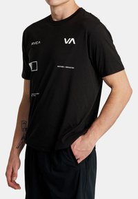 Čierne tričko s krátkymi rukávmi, s bielymi grafickými potlačami vrátane textu a tvarov. Vyrobené z jemného materiálu, vo voľnom strihu.