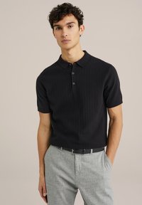 Polo negru cu dungi, cu mâneci scurte, guler clasic și deschidere cu două nasturi. Purtați cu pantaloni gri deschis și un brâu negru.