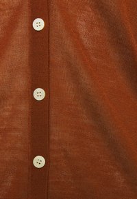 Brązowy sweter z dzianiny z dekoltem w kształcie litery V, sześcioma guzikami z przodu i lekko teksturowanym materiałem.