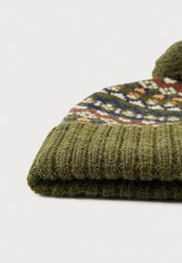 Kootud roheline beanie, mille ülaosas on dekoratiivne värviline muster ja alumises osas tekstureeritud soonik.