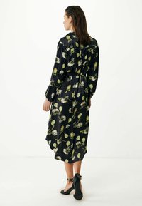 Svart blommig klänning med gröna och vita blommönster, långa ärmar och ett bälte i midjan. Flödande tyg och längden når ankeln.