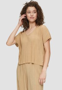 Korte mouw V-hals top in een lichtbruine geplooide stof, met een ontspannen pasvorm en subtiele glans. Soepele textuur met een nette zoom.