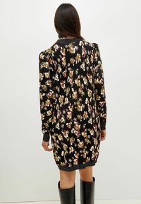 Robe noire à fleurs avec une finition texturée, arborant des motifs floraux multicolores, des manches longues et des accents côtelés aux poignets et à l'ourlet.