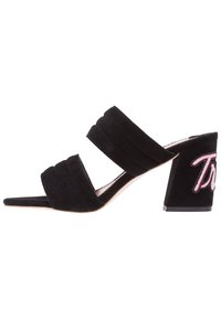 Černé semišové sandály na vysokém podpatku s dvěma širokými pásky, zúženým otevřeným špičkou a masivním podpatkem, na kterém je vyšitý růžový nápis.