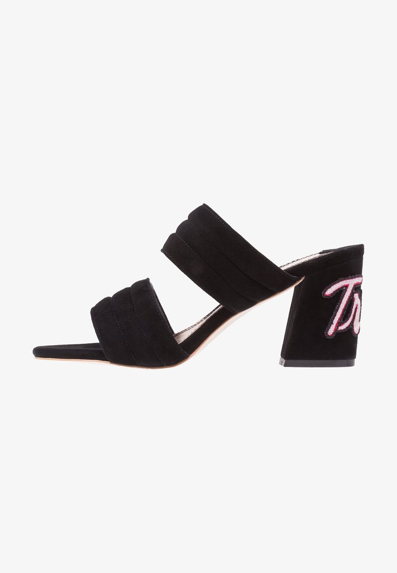 Černé semišové sandály na vysokém podpatku s dvěma širokými pásky, zúženým otevřeným špičkou a masivním podpatkem, na kterém je vyšitý růžový nápis.