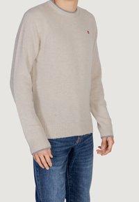 Helles beiges Sweatshirt mit Rundhalsausschnitt und gerippten Bündchen, das an Ausschnitt und Saum mit einem kontrastierenden blauen Akzent versehen ist. Weiche Textur.