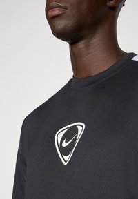 Czarna koszulka sportowa z białym logo Nike na klatce piersiowej, o okrągłym dekolcie i gładkiej fakturze materiału.