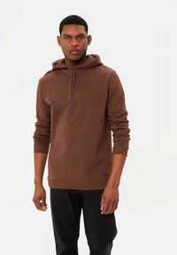 Brauner Kapuzenpullover aus weichem Stoff mit einer strukturierten Kordel und einem kleinen Logo auf der Brust. Mit gerippten Bündchen und Saum.
