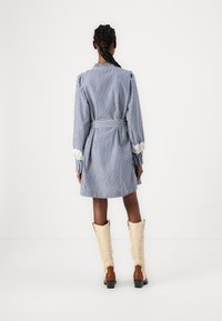 Mėlyna ir balta dryžuota suknelė su ilgomis rankovėmis ir nėriniais, per juosmenį surišta diržu. Dėvima su grietinėlės spalvos kaubojiškais batais su rudos spalvos detalėmis.