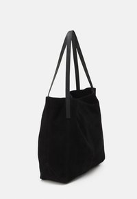 Sac fourre-tout en suède noir avec deux longues poignées plates et un design souple et non structuré. Présente des coutures visibles et une ouverture spacieuse.