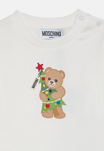 Бяла бебешка риза с етикет Moschino и мече, държащо украсена коледна елха с цветни украшения и червена звезда.