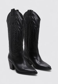 Bottes de cowboy en cuir noir avec des bouts pointus, un petit talon carré et des motifs de couture complexes le long de la tige.