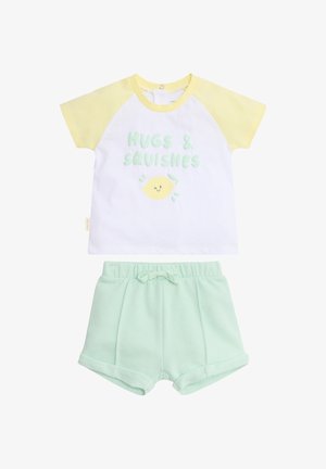 Camiseta de manga corta para niño pequeño con mangas amarillas y texto "Abrazos y achuchones" sobre un limón sonriente, combinada con pantalones cortos de cintura elástica color verde menta.