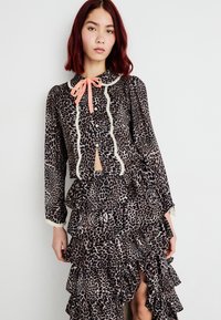 Leopardmønstret bluse med krave, lyserød båndsløjfe og blondestik. Den matchende volangskørt har flere lag og en sideslids.