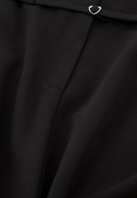 Zwart stof met een gladde textuur, voorzien van een kleine zilveren hardware accent en een vouwdetail bij de tailleband.