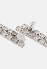 Bracelet en argent composé de maillons rectangulaires entrelacés avec des pierres claires. Le fermoir présente un dessus arrondi et un détail de fermeture circulaire.