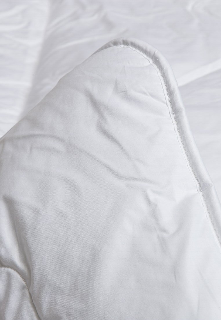 Weißes Kissen mit einem glatten, weichen Stoffbezug, der einen dezenten Glanz und saubere Nähte entlang der Kanten aufweist, auf einer weißen Oberfläche liegend.