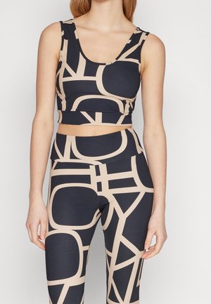 Vrouw draagt een mouwloos crop top met een zwart-beige geometrisch patroon en bijpassende hooggetailleerde leggings.