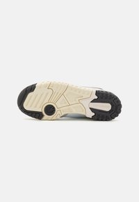 Shoe outsole featuring a textured rubber tread, beige midsole, and black heel. Includes a circular logo detail and distinct traction grooves.