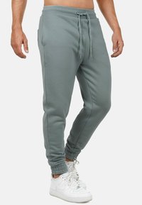 Grijze joggingbroek met elastische tailleband, aanpasbare trekkoord, zijzakken en elastische boorden. Draagt met witte sneakers.