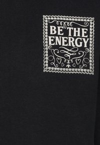 Zwarte stof heeft een witte bedrukte graphic met de tekst "WEES DE ENERGIE" in een ingewikkeld randontwerp, met decoratieve elementen.