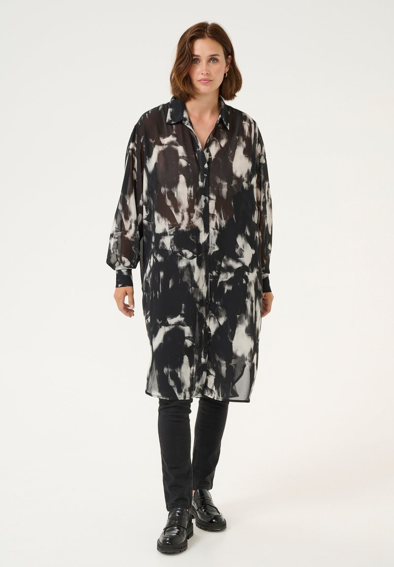 Schwarz-weiß gemustertes Longsleeve-Hemdkleid aus transparentem Stoff mit Knopfleiste, ergänzt durch einen klassischen Kragen und Manschetten.
