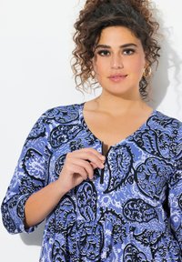 Vestido de estampado azul y negro con escote en V, mangas tres cuartos y una falda fruncida con un detalle de cremallera central.