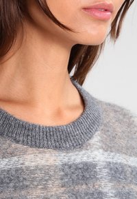 Harmaa neulepaita, jossa on resorinen pä�äntie, pehmeä koostumus ja hienovaraiset värivaihtelut, yhdistäen vaaleita ja tummia harmaan sävyjä.