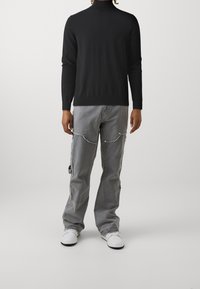 Czarny golf w połączeniu z szarymi spodniami cargo z bocznymi kieszeniami i srebrnymi detalami. Całość dopełniają białe trampki.