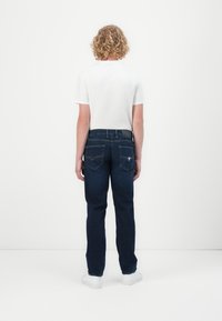 Blue denim jeans with a straight-leg fit, five pockets, and a white T-shirt; minimal stitching detail on back pockets. White shoes.