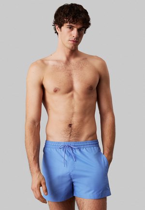 Costumi da bagno azzurri chiari con vita elastica, dettaglio con cordoncino e tasche laterali; realizzati in tessuto morbido e leggero.