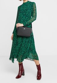 Zielona sukienka w panterkę z długimi, przezroczystymi rękawami, uzupełniona czarną prostokątną torebką i błyszczącymi burgundowymi botkami za kostkę.