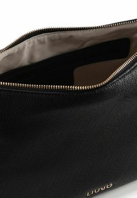 Zwarte leren tas met een gestructureerde afwerking, voorzien van een gouden rits en een beige voering. Logo in reliëf aan de zijkant.