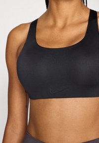 Zwarte sportbeha met een gladde textuur, brede schouderbanden en een subtiel Nike-logo in het midden, ontworpen voor actief gebruik.