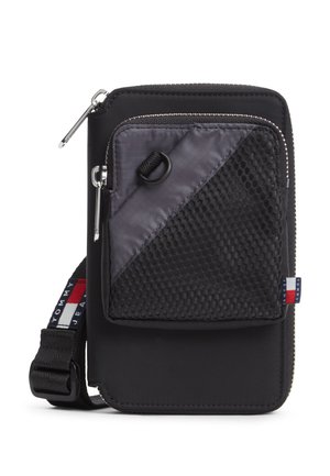 Czarna nylonowa saszetka na ramię z przednią kieszenią z siateczki zapinaną na zamek, regulowanym paskiem i małą czerwono-biało-niebieską metką z logo Tommy Jeans.