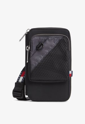 Czarna nylonowa saszetka na ramię z przednią kieszenią z siateczki zapinaną na zamek, regulowanym paskiem i małą czerwono-biało-niebieską metką z logo Tommy Jeans.