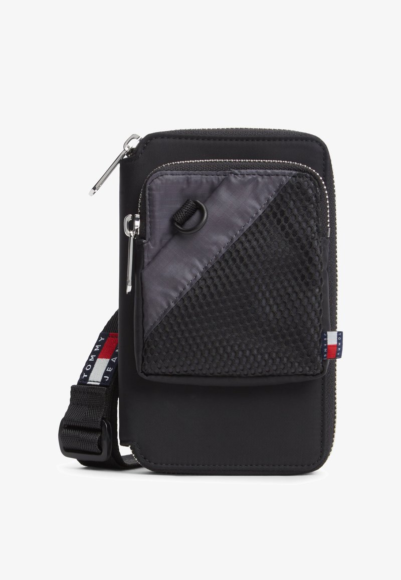 Pochette bandoulière en nylon noir avec poche avant en mesh zippée, sangle réglable et petite étiquette logo Tommy Jeans rouge, blanche et bleue.