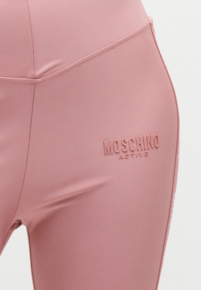 Κοντινή λήψη ροζ κολαν Moschino Active με ανάγλυφο λογότυπο στο πάνω μέρος του μηρού, με ορατές ραφές και λεπτομέρειες ραφών.