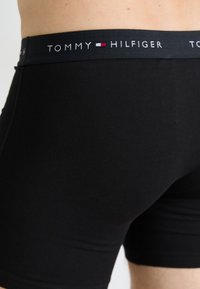 Boxers noirs en tissu doux, avec une ceinture élastique de marque dans une couleur sombre avec un texte blanc et un petit motif accentué.
