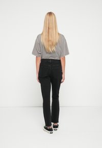 Camiseta gris de gran tamaño combinada con vaqueros ajustados negros. Zapatos negros con suela blanca. Se ve pelo largo rubio desde atrás.