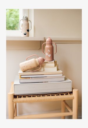 Tři láhve na vodu v pastelových barvách: růžová s motivem listu, béžová s květinovými akcenty a vzorovaná láhev na hromadě knih.