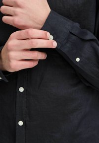 Sötétkék lening póló gombos mandzsettával. A póló finom textúrával rendelkezik, és standard gombos rögzítéssel van ellátva, kontrasztos világos színben.