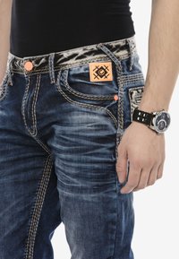 Dunkelblaue Jeans aus Denim mit kontrastierendem orangen Nähten, einem gemusterten schwarz-weißen Bund und einem Logo-Patch auf der Vorderseite.