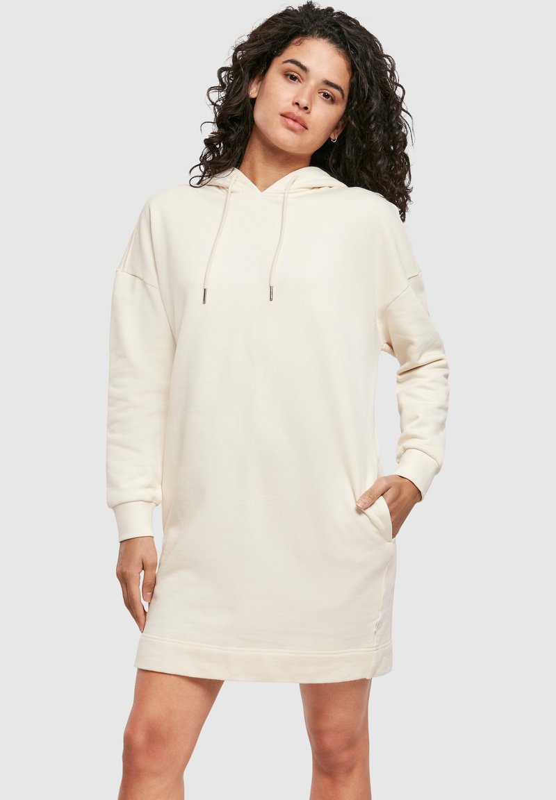 Vestito con cappuccio color crema realizzato in tessuto morbido. Presenta una tasca frontale, maniche lunghe e coulisse regolabili sul cappuccio.
